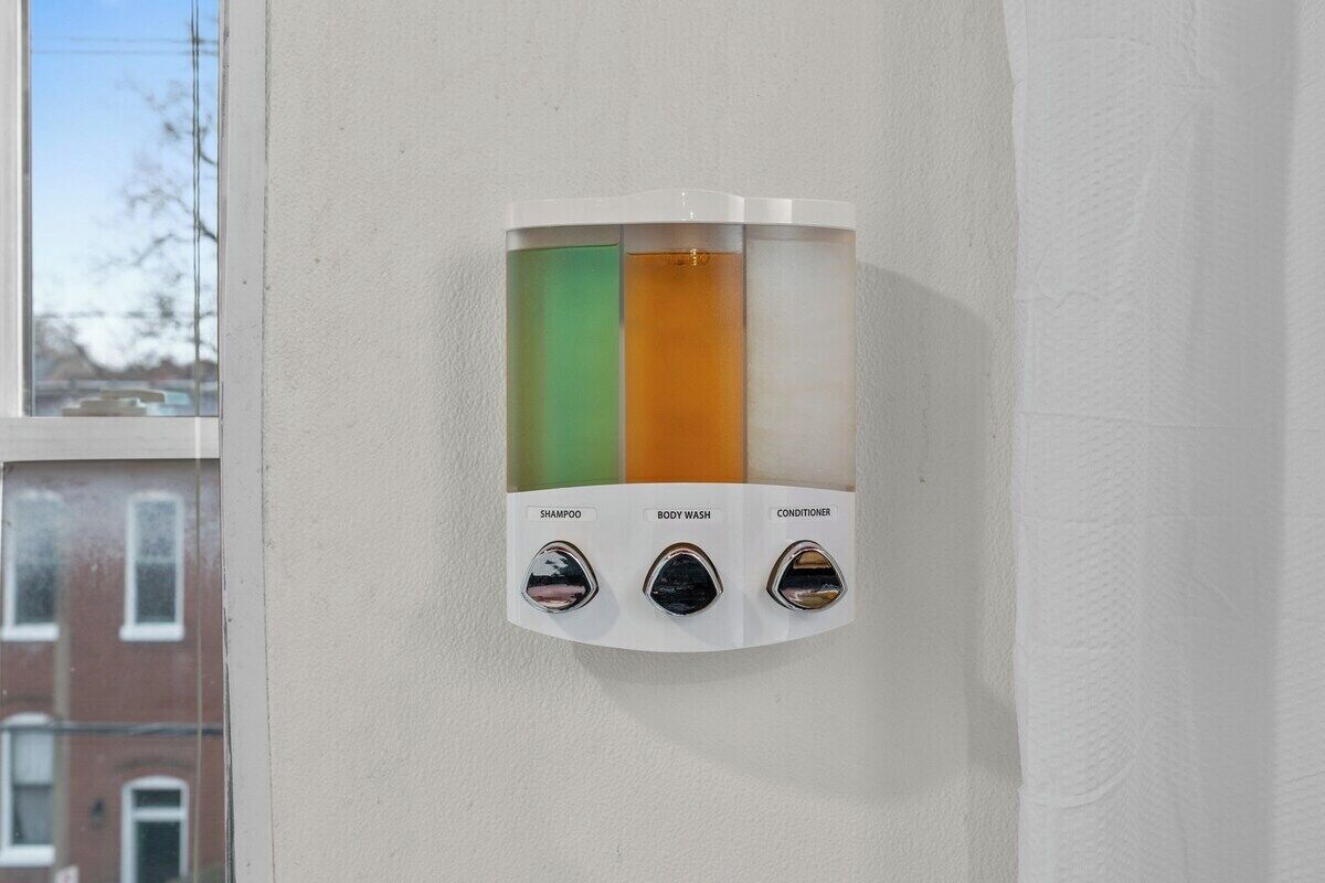 A wall-mounted dispenser with three compartments labeled shampoo, body wash, and conditioner.