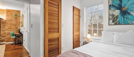 Un dormitorio con una cama grande, puertas de madera, una ventana con persianas y un cuadro en la pared.