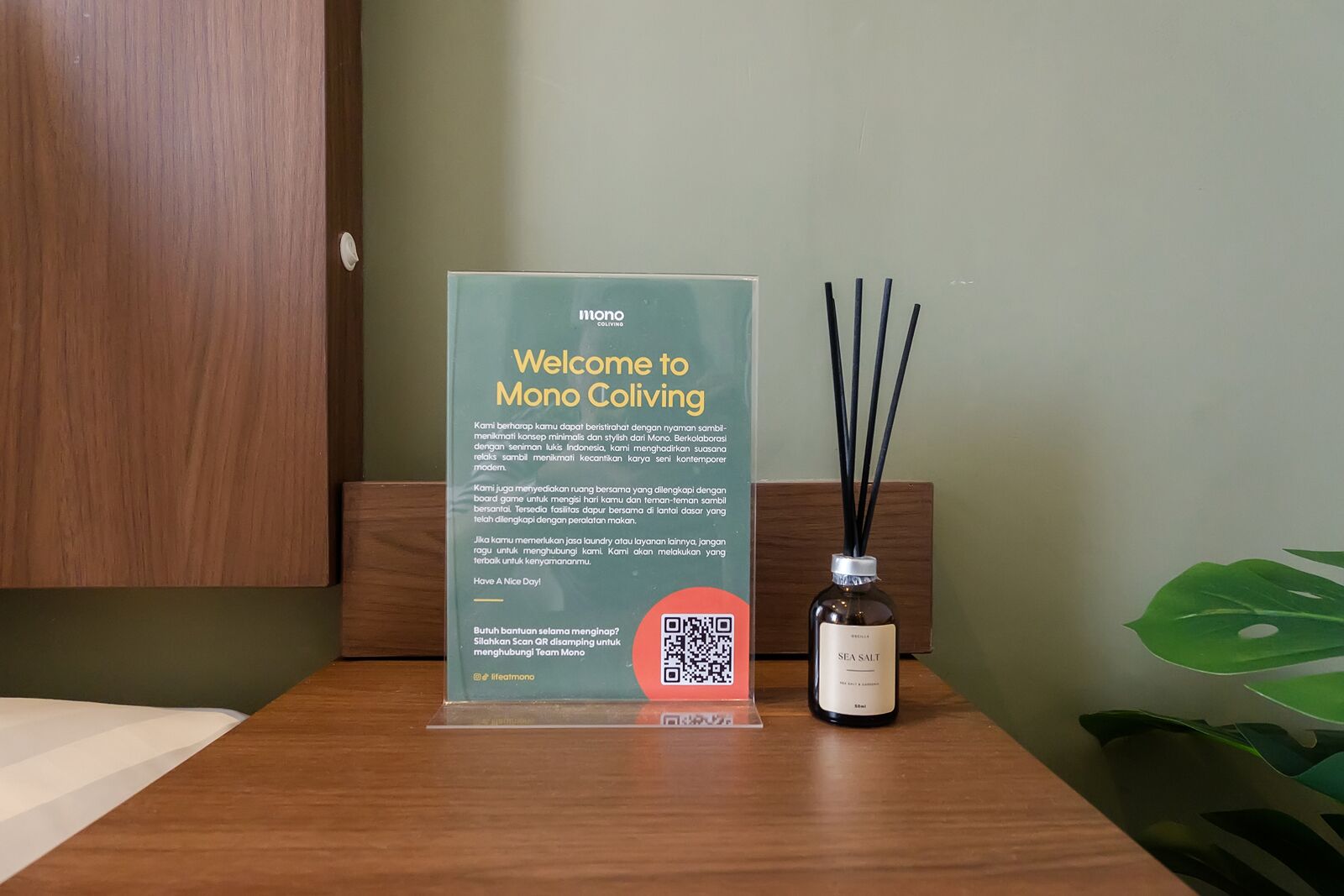 A welcome sign for Mono Coliving with a QR code, a bottle of sea salt, and a plant.