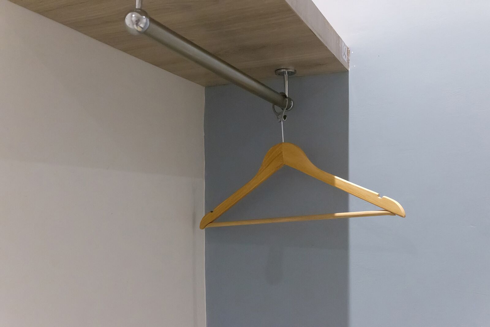 Ein hölzerner Kleiderbügel hängt an einer Deckenstange in einem Raum mit hellgrauen Wänden.
