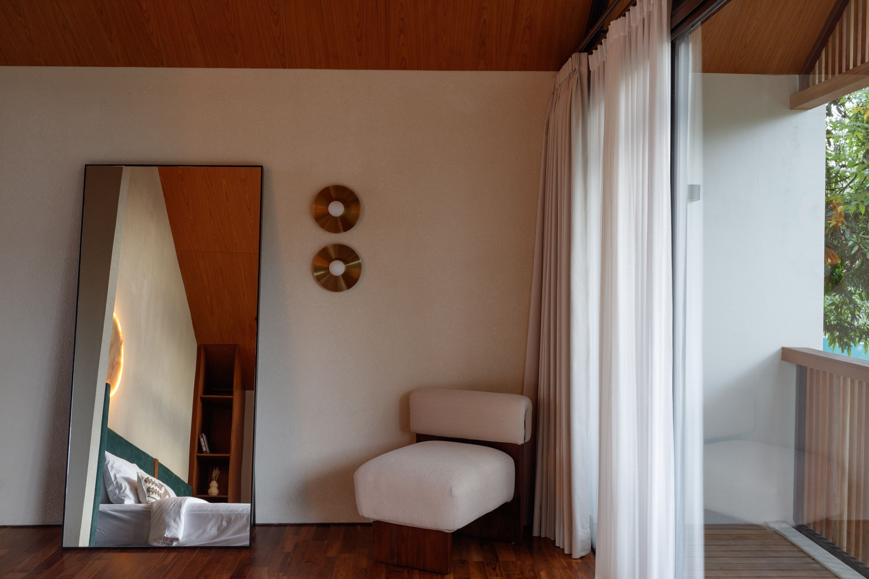 A modern room with a large mirror, a small seating area, and a view of greenery outside.
