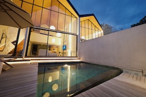 Une maison moderne dotée d’un salon entièrement vitré, d’une terrasse en bois et d’une piscine.