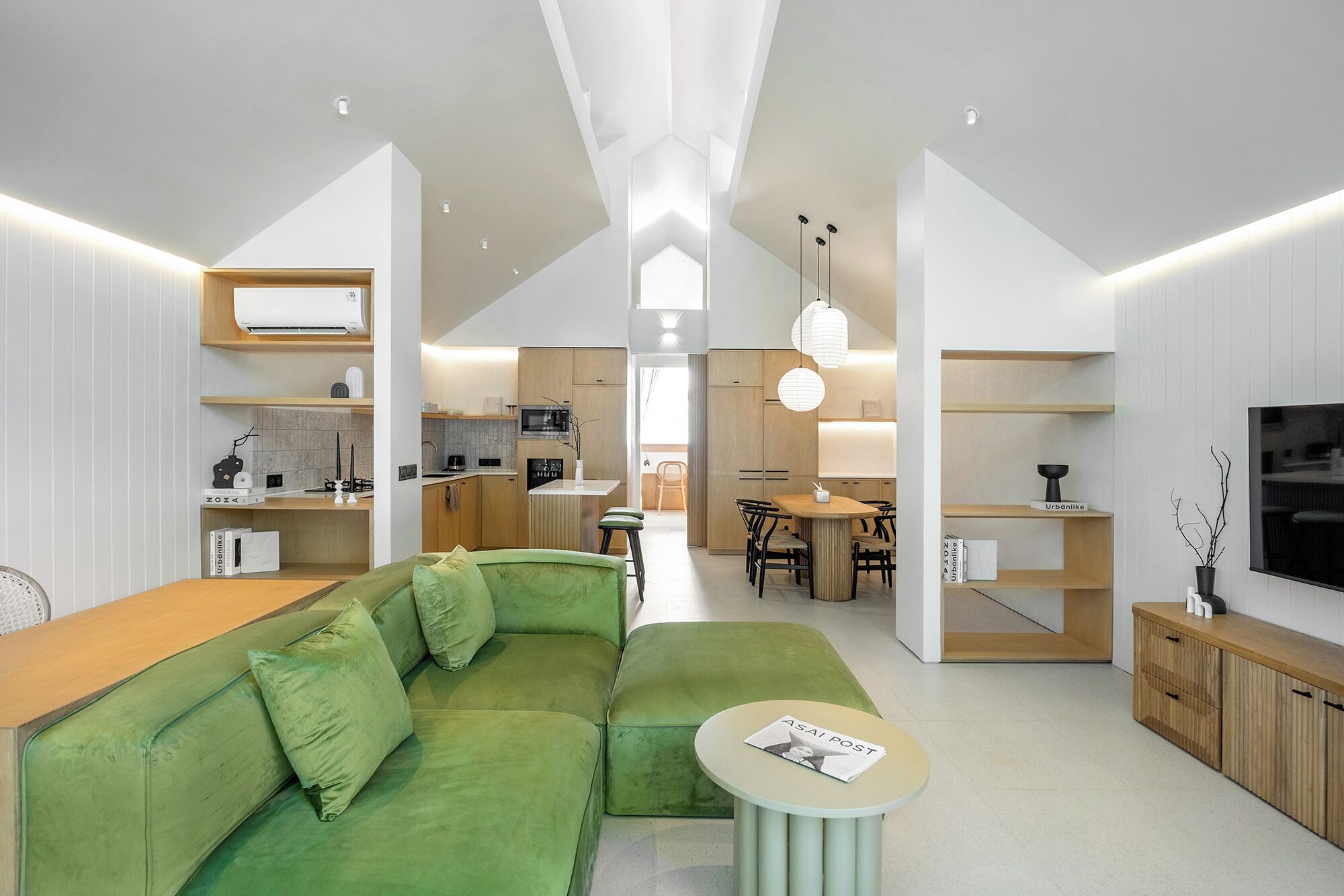 A modern living room with a green sofa, a small round table, and a kitchen in the background.