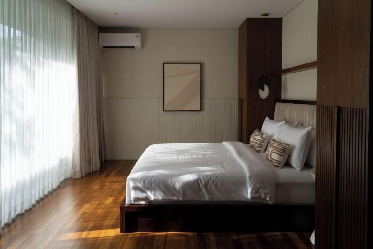 Un dormitorio con una cama, una ventana con cortinas, un equipo de aire acondicionado y un cuadro en la pared.