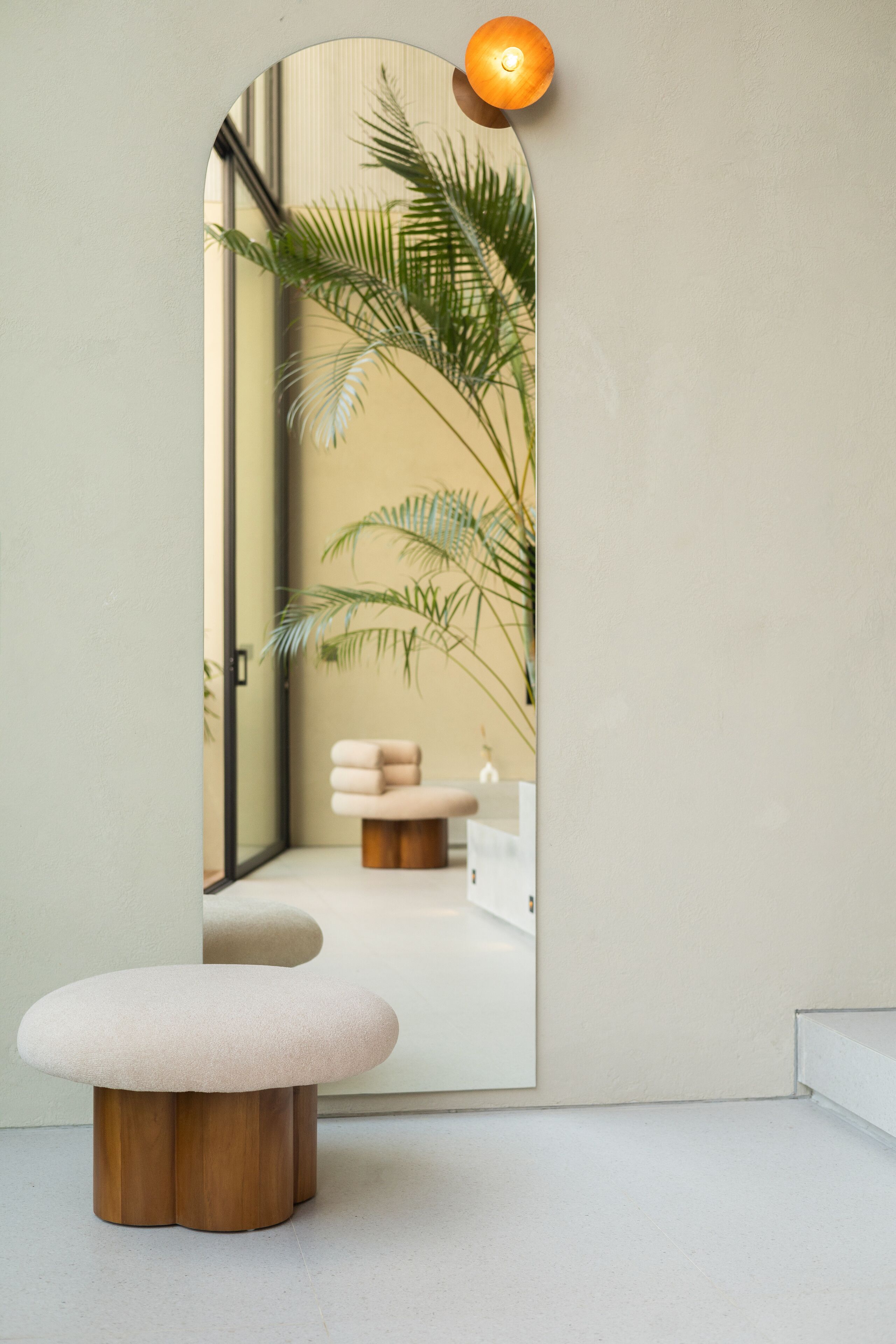 A minimalist room with a round wooden stool, a small round table, and a potted plant.