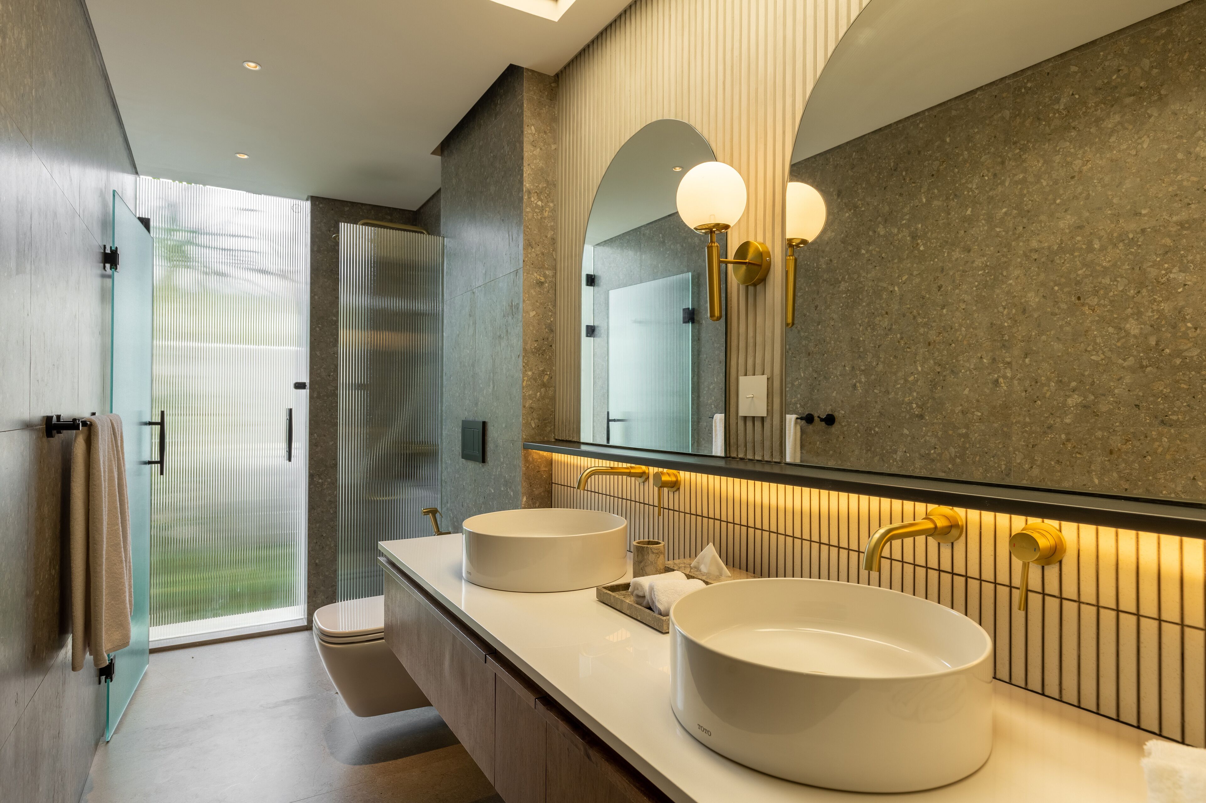 Une salle de bain moderne avec deux grands lavabos, une douche en verre et un grand miroir agrémenté de luminaires fixés au mur.