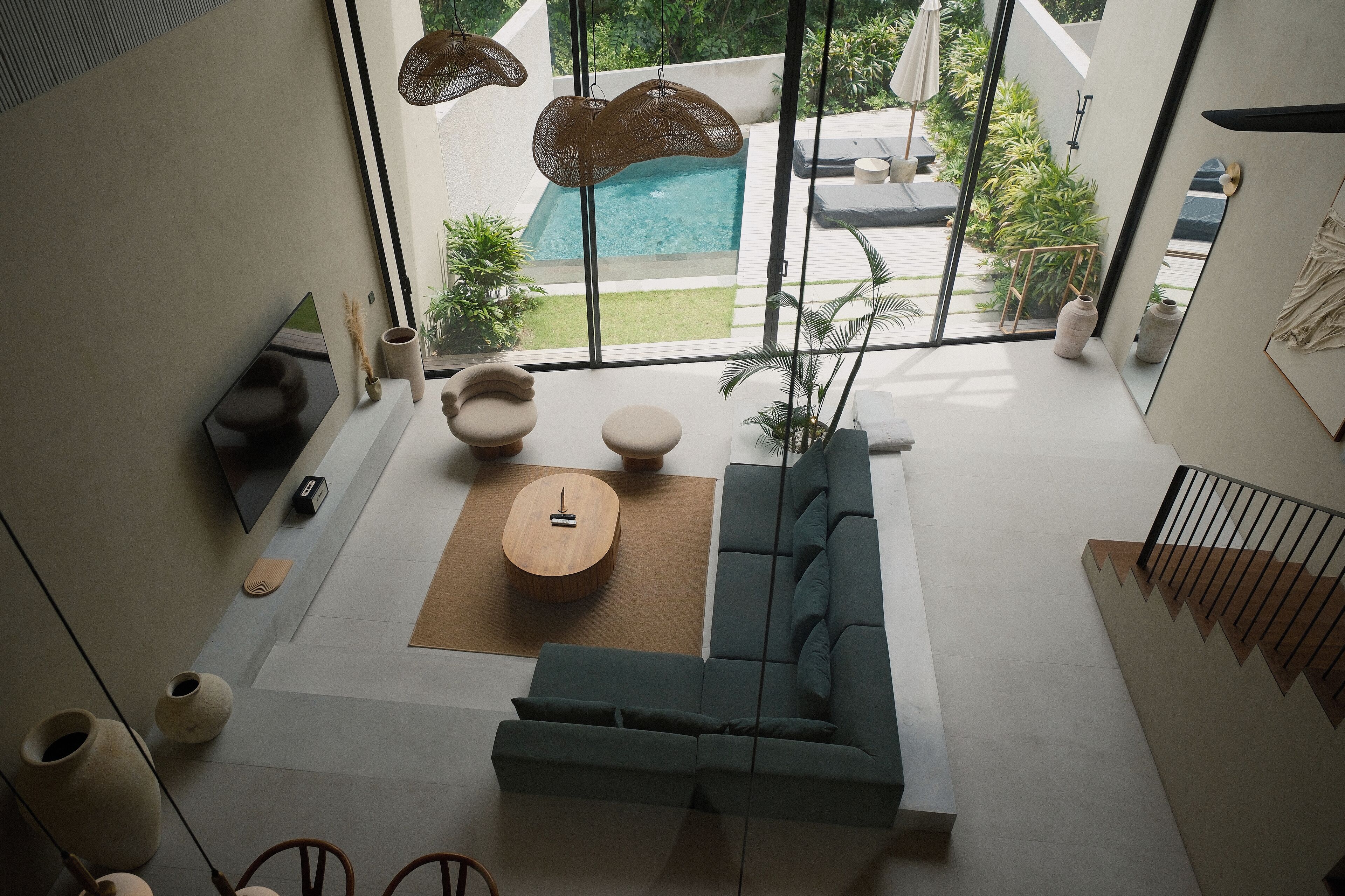 A modern living room with a large window, a sofa, a coffee table, and a view of a swimming pool.