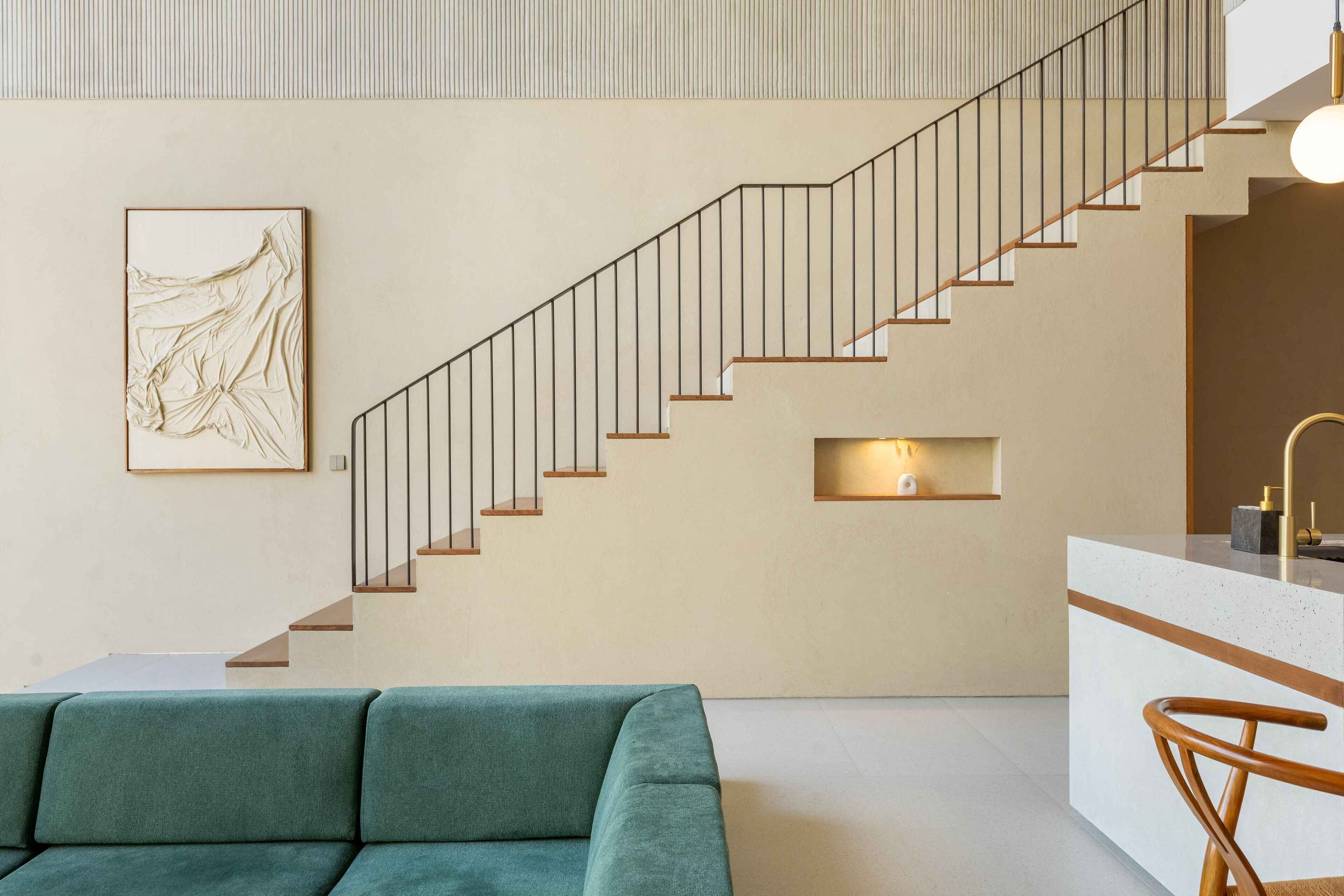 A modern interior with a staircase, a green sofa, and a kitchen area.