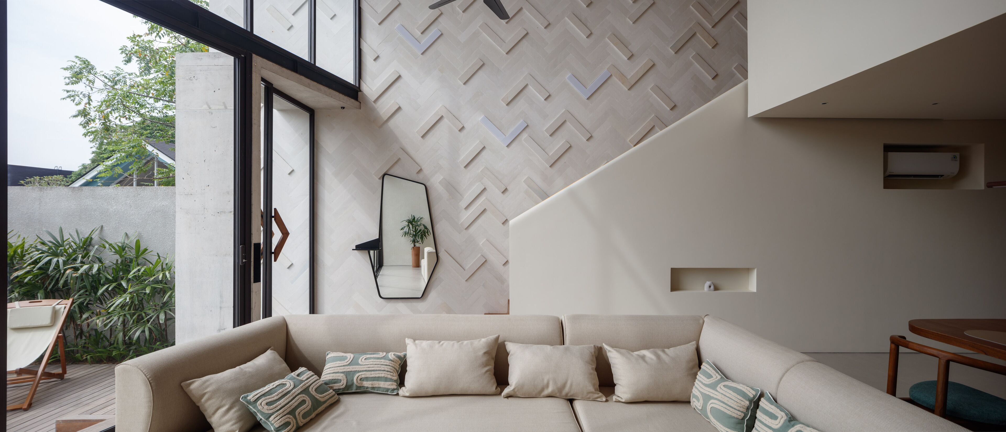 Un salon moderne avec un canapé, un miroir et un mur orné d’un motif en chevrons.