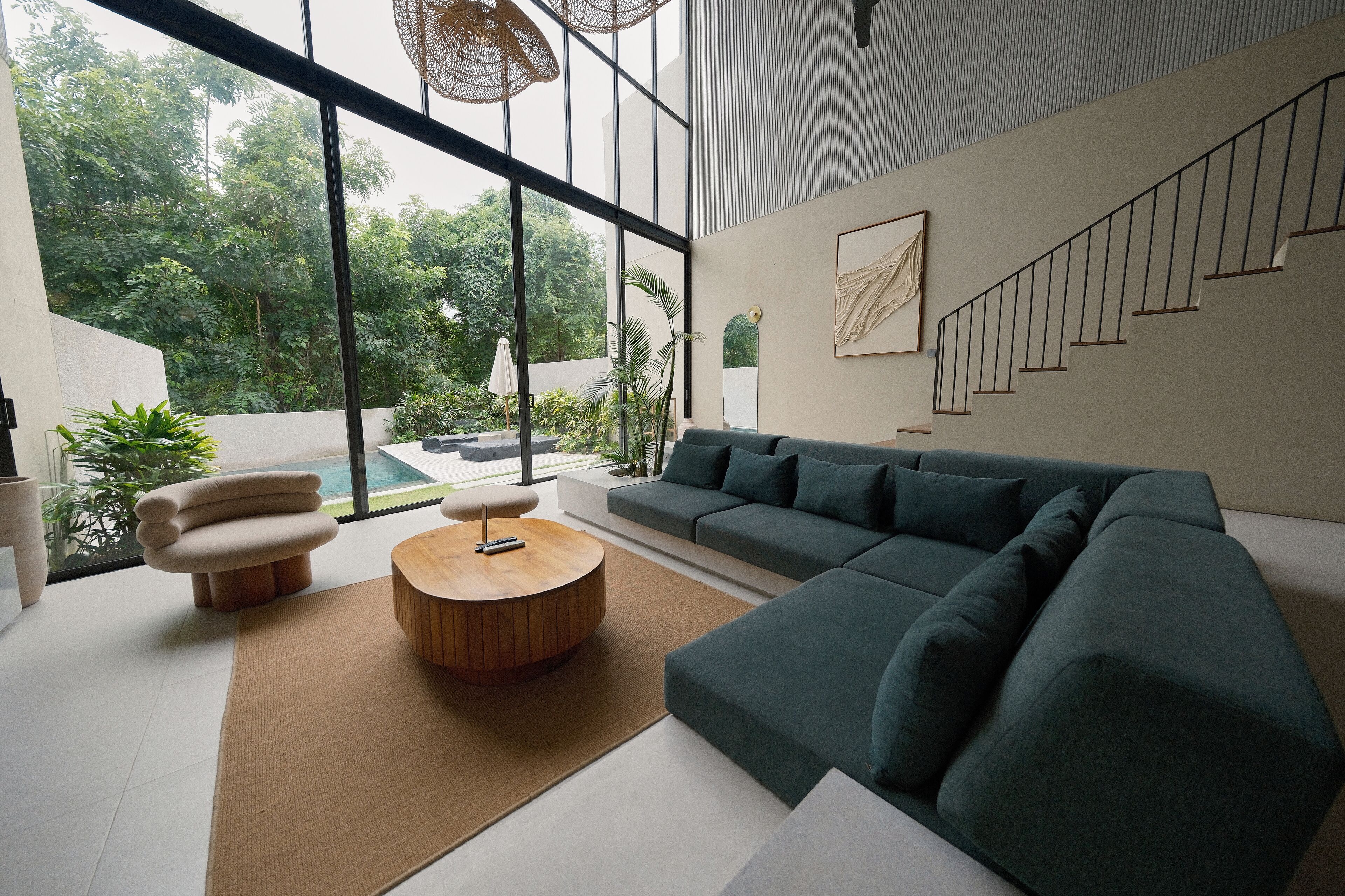 A modern living room with a sectional sofa, a round wooden coffee table, and a large window overlooking a garden.