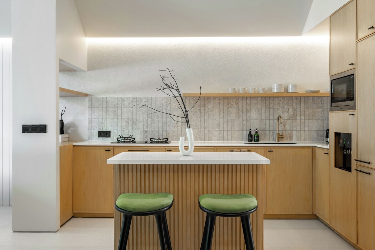 Una cocina moderna con armarios de madera, encimera blanca y dos taburetes verdes.