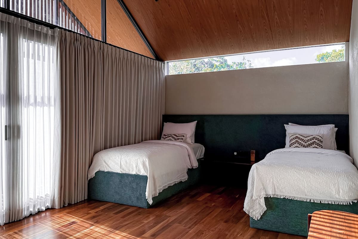 A modern bedroom with two beds, wooden flooring, and a large window with curtains.
