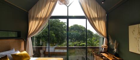 A bedroom with a large window, a bed with a patterned bedspread, a desk, and a chair.