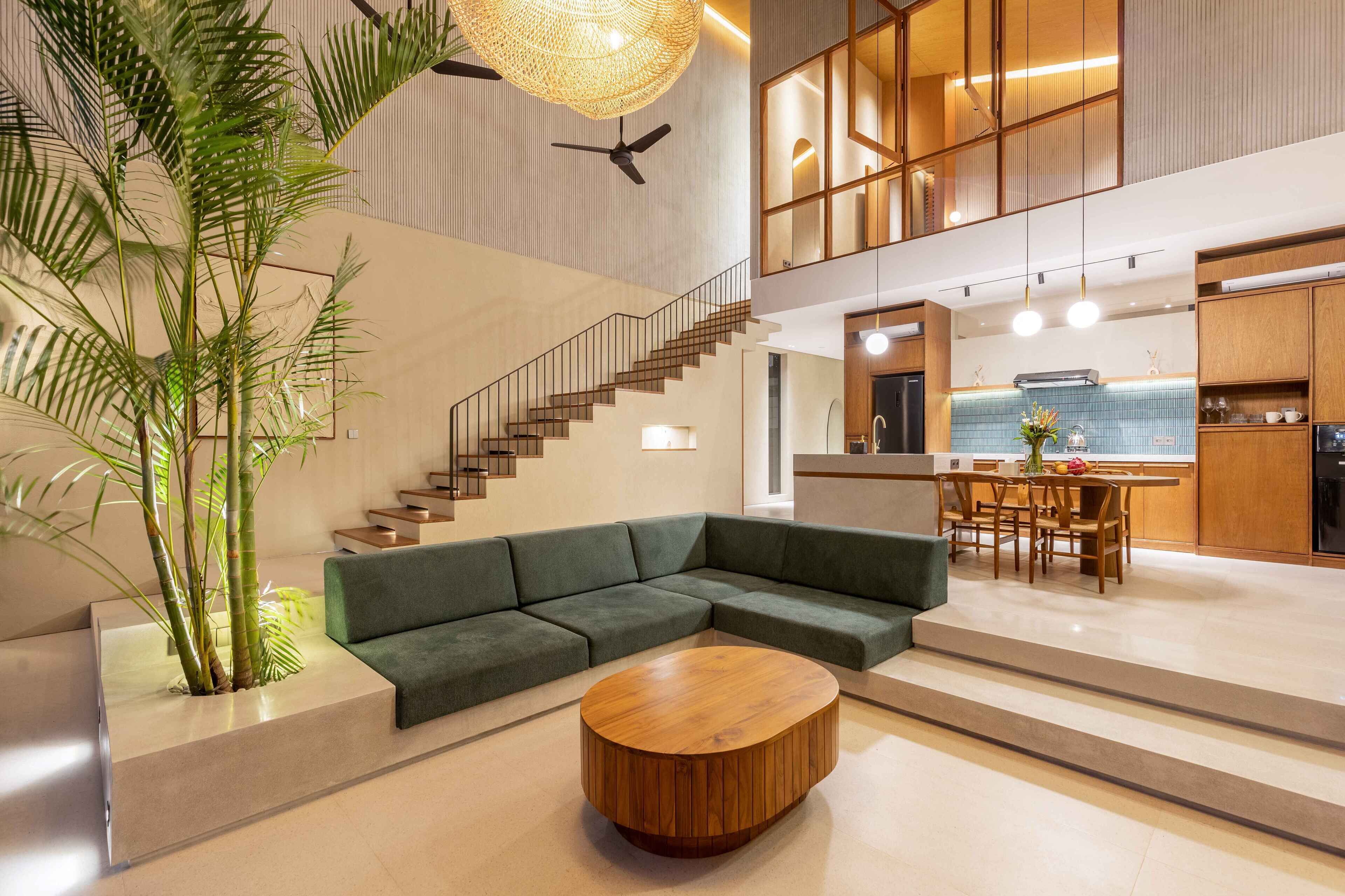 A modern interior with a green sectional sofa, a wooden coffee table, and a staircase leading to an upper level.