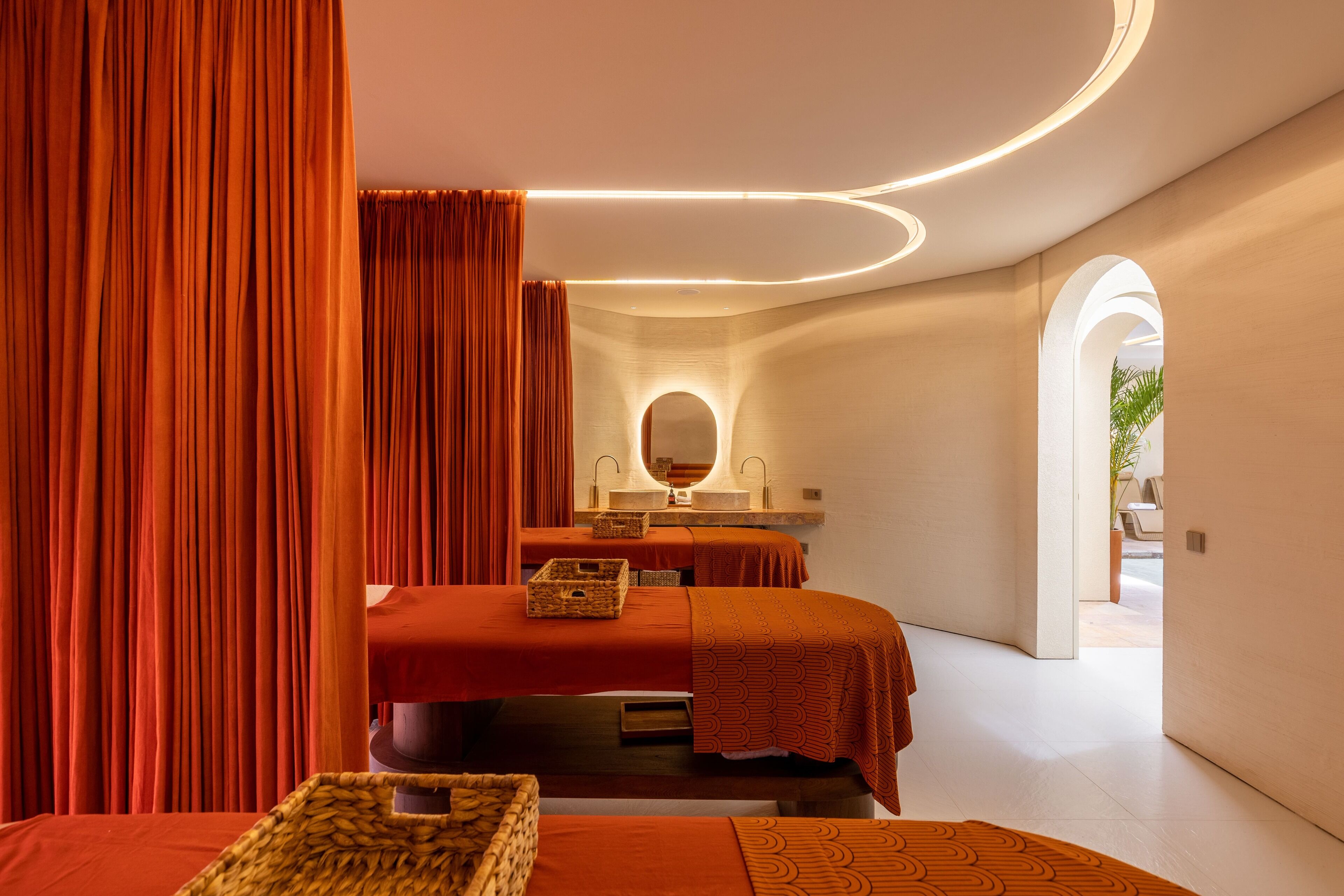 A modern spa room with two beds, a large mirror, and a sink.