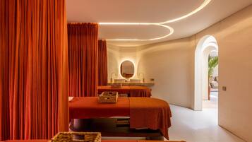 A modern spa room with two beds, a large mirror, and a sink.