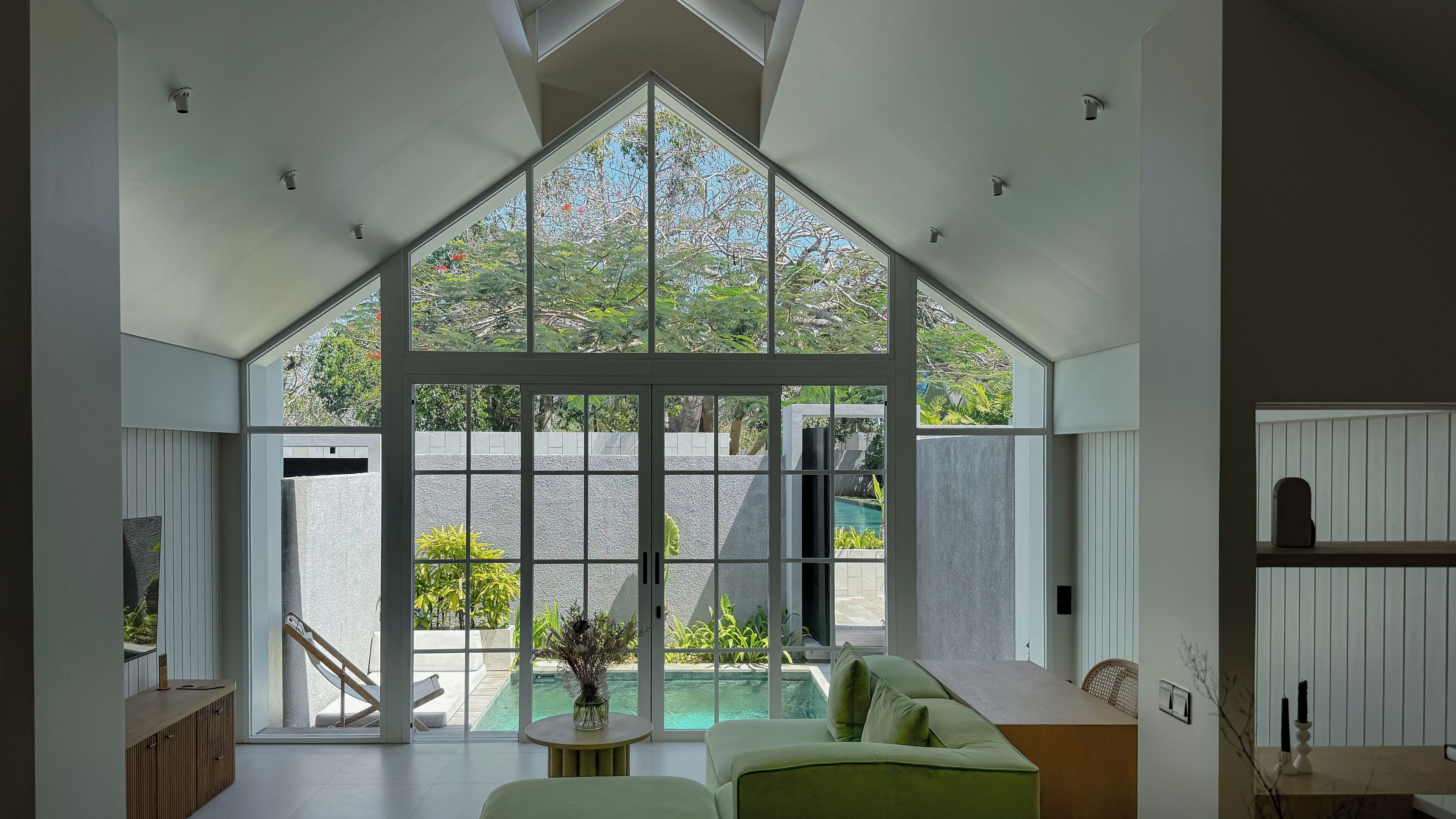 Una habitación amplia con un gran ventanal, una piscina y un sofá verde.