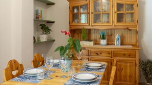 Un coin repas avec une table en bois dressée pour quatre personnes, entourée de chaises. On y trouve de la verrerie et des assiettes, et un buffet avec des portes en verre au-dessus.
