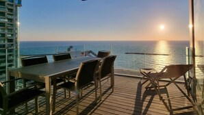 Een terras met tafel en stoelen met uitzicht op de oceaan bij zonsondergang.