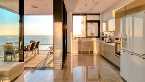 Een moderne keuken met uitzicht op zee, een eethoek met tafel en stoelen, en een grote schuifpui die uitkomt op een balkon.
