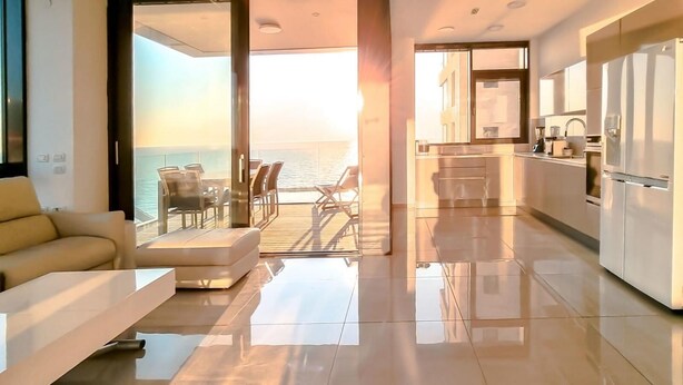 Een modern interieur met een bank, eettafel en stoelen, nabij een groot raam met uitzicht op zee.