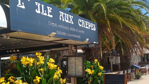 Un stand de crêpes installé au bord de la rue, avec une enseigne qui fait de la publicité pour « L’ÎLE RUX CREPES ».