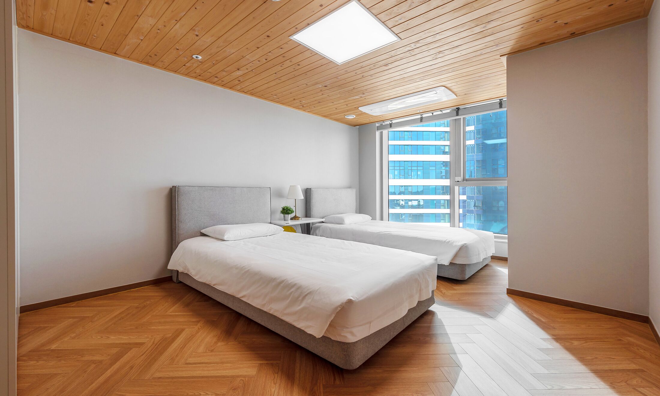 Une chambre moderne avec deux lits, un plancher en bois et de grandes fenêtres donnant sur la ville.