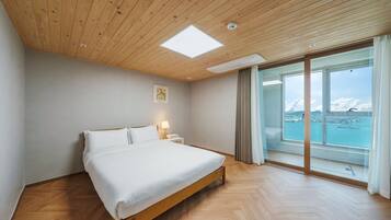 A bedroom with a bed, a nightstand, a lamp, a ceiling light, and a large window with a view of a body of water and a bridge.