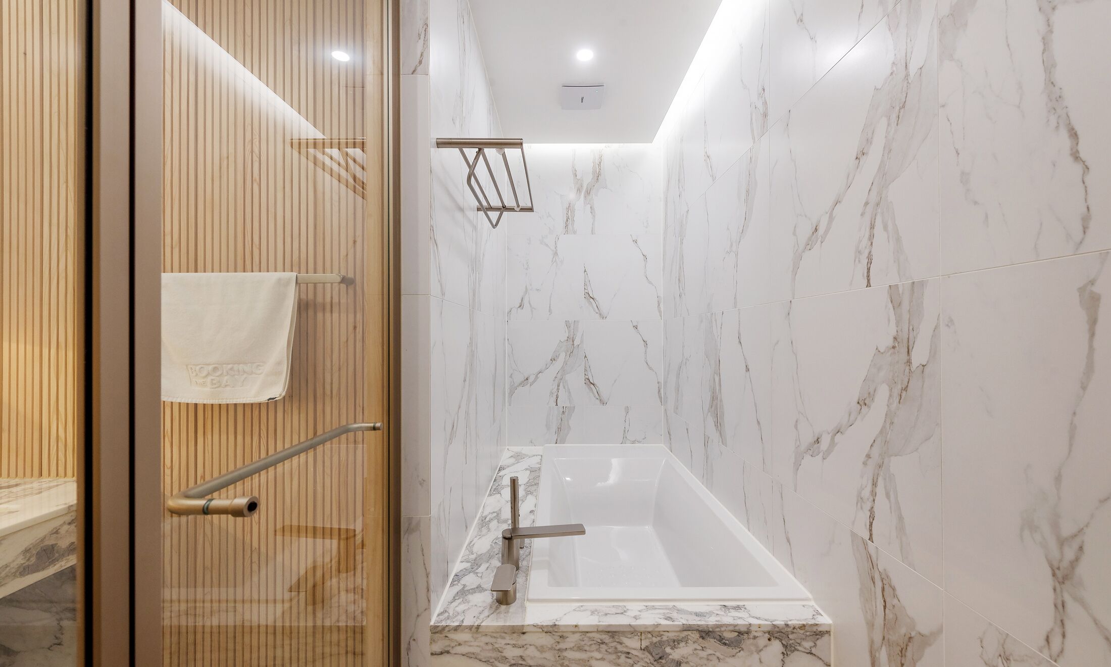 Un baño moderno con pared de mármol, una bañera y un perchero para toallas.