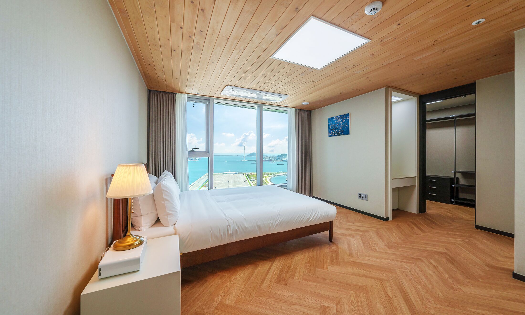 Una habitación de hotel con una cama grande, un escritorio con lámpara, un armario y vista al mar.