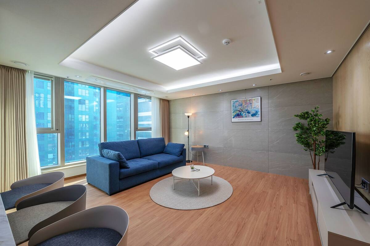 Uma sala de estar moderna com um sofá azul, uma mesa de centro redonda e uma televisão de tela plana.