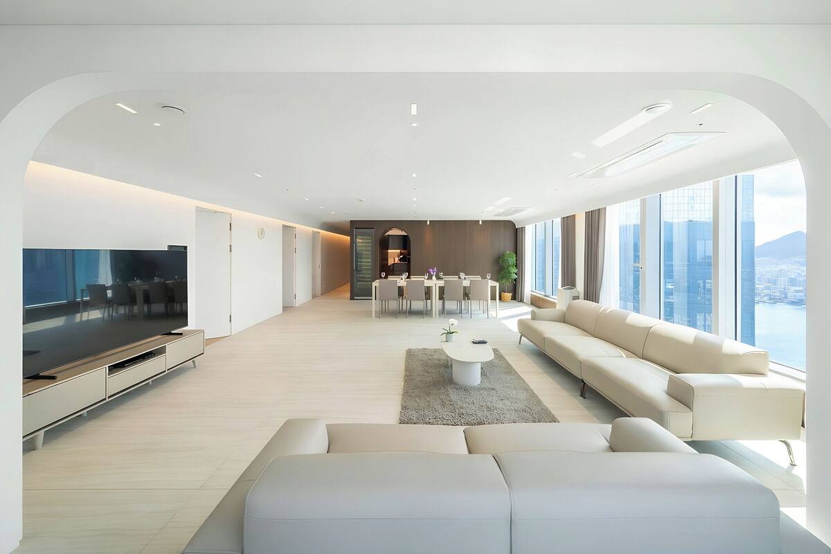 Uma sala de estar moderna com uma televisão grande, um sofá, uma mesa de centro e uma área de jantar com cadeiras.