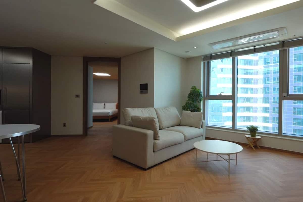 Uma sala de estar moderna com um sofá, uma mesinha redonda e vista para o horizonte urbano através de grandes janelas.