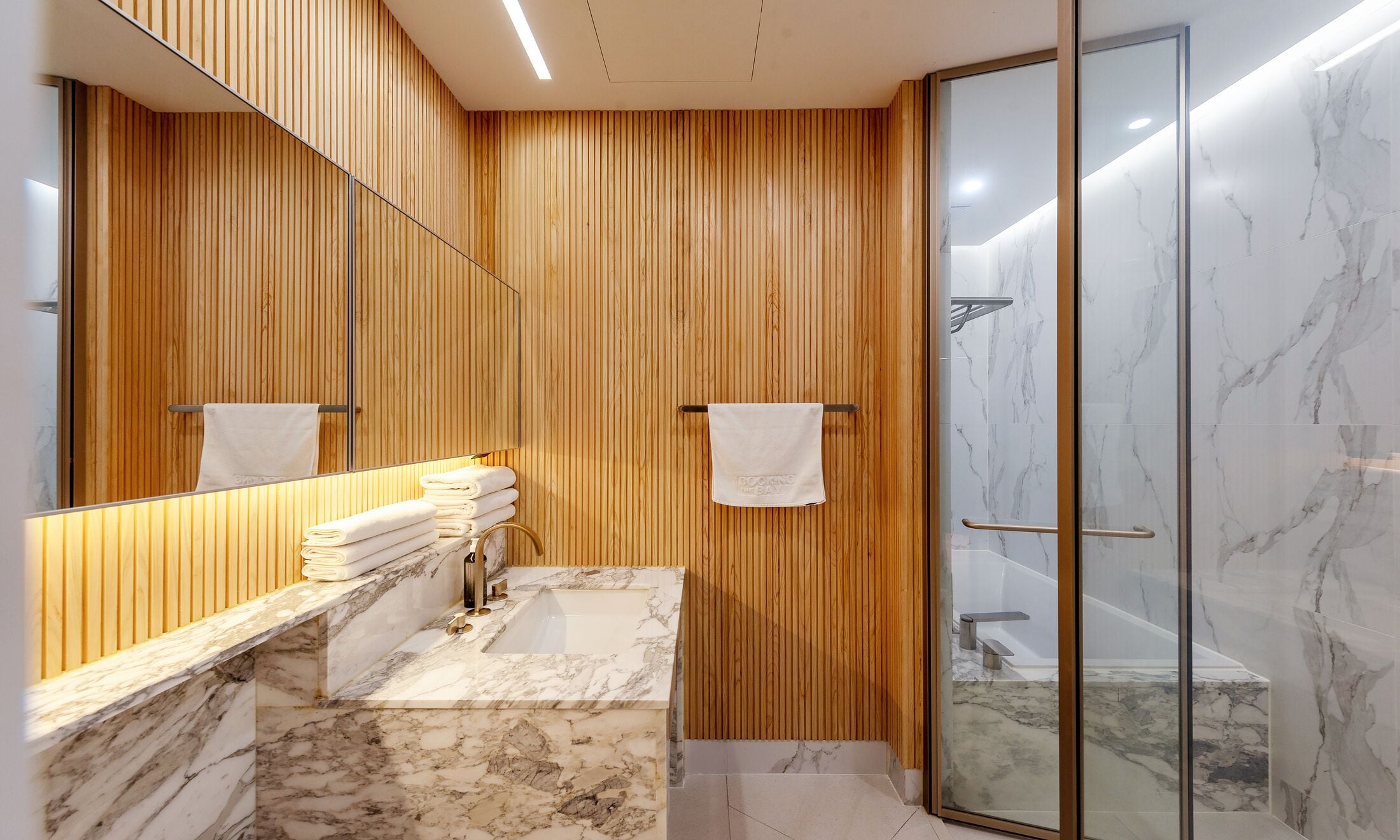 A modern bathroom with wooden paneling, a marble sink, and a glass-enclosed shower.