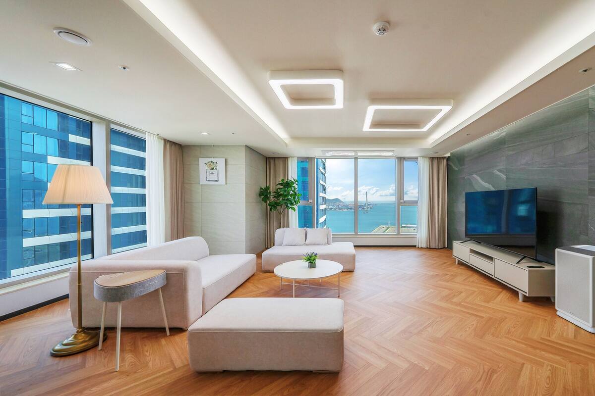 Sala de estar moderna com sofá, apoio para os pés, televisão e uma grande janela com vista para a cidade.