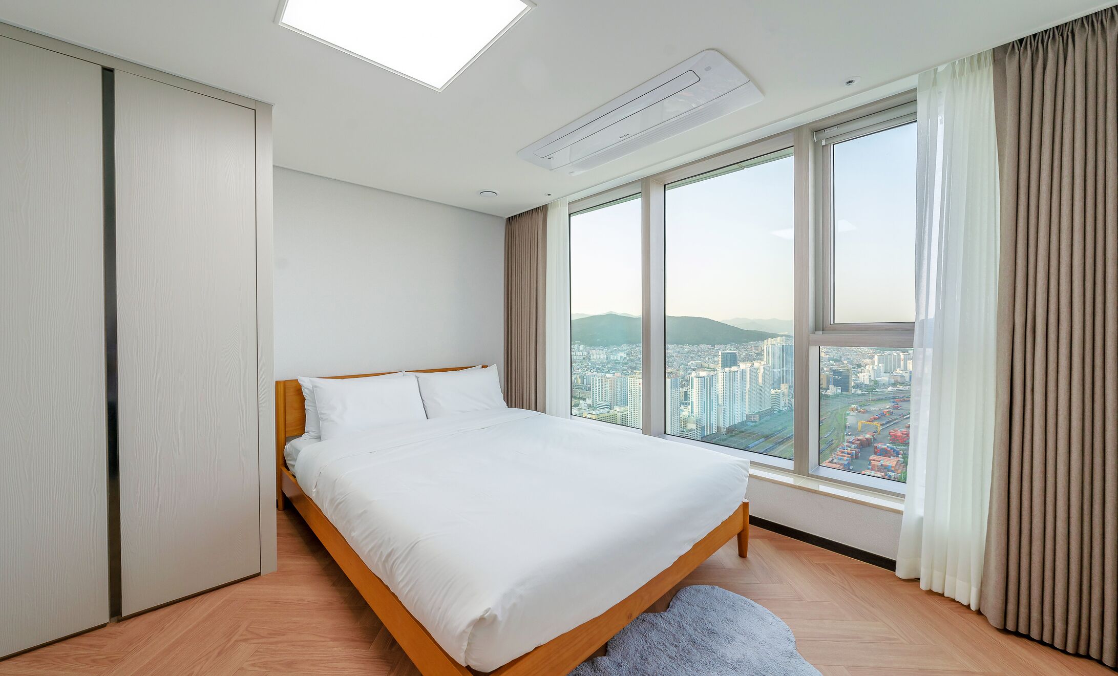A modern hotel room with a large bed, a skylight, and a city view.