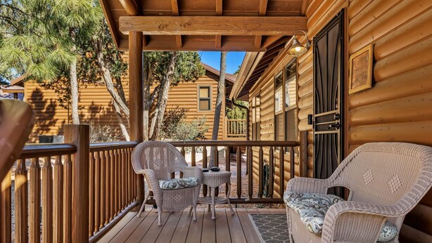 Una terraza de madera con mobiliario de mimbre y una puerta a una cabaña de troncos.