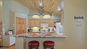 Una cocina con armarios de madera, encimera de granito, microondas y dos taburetes rojos.