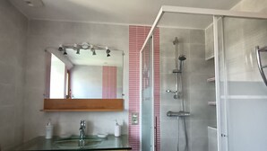 Un baño con cabina de ducha de vidrio, tocador de madera con lavamanos de vidrio y un espejo sobre el lavamanos.