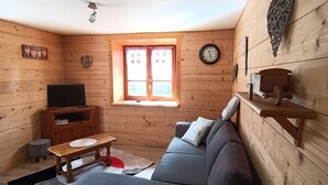 Una cabaña de madera acogedora con sofá, televisión, una mesita y una ventana con cortinas.