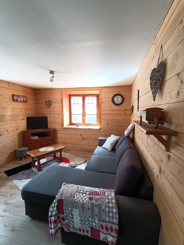 A cozy wooden cabin with a sofa, a television, a small table, and a window with curtains.
