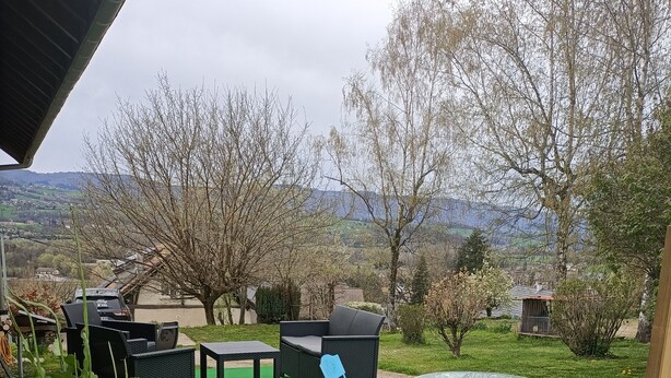 Un patio al aire libre con césped artificial verde, una mesa redonda, sillas plegables azules y un sofá de mimbre.
