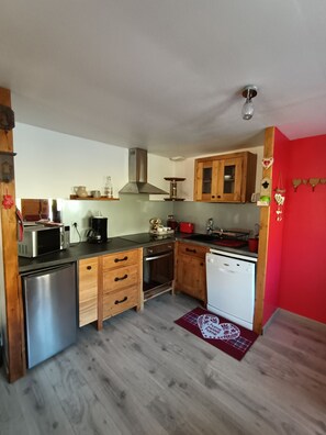 A compact kitchen with wooden cabinets, a stainless steel refrigerator, a dishwasher, and a microwave.