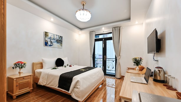 Habitación de hotel con cama, mesita de noche, lámpara y escritorio con computadora portátil y cafetera.
