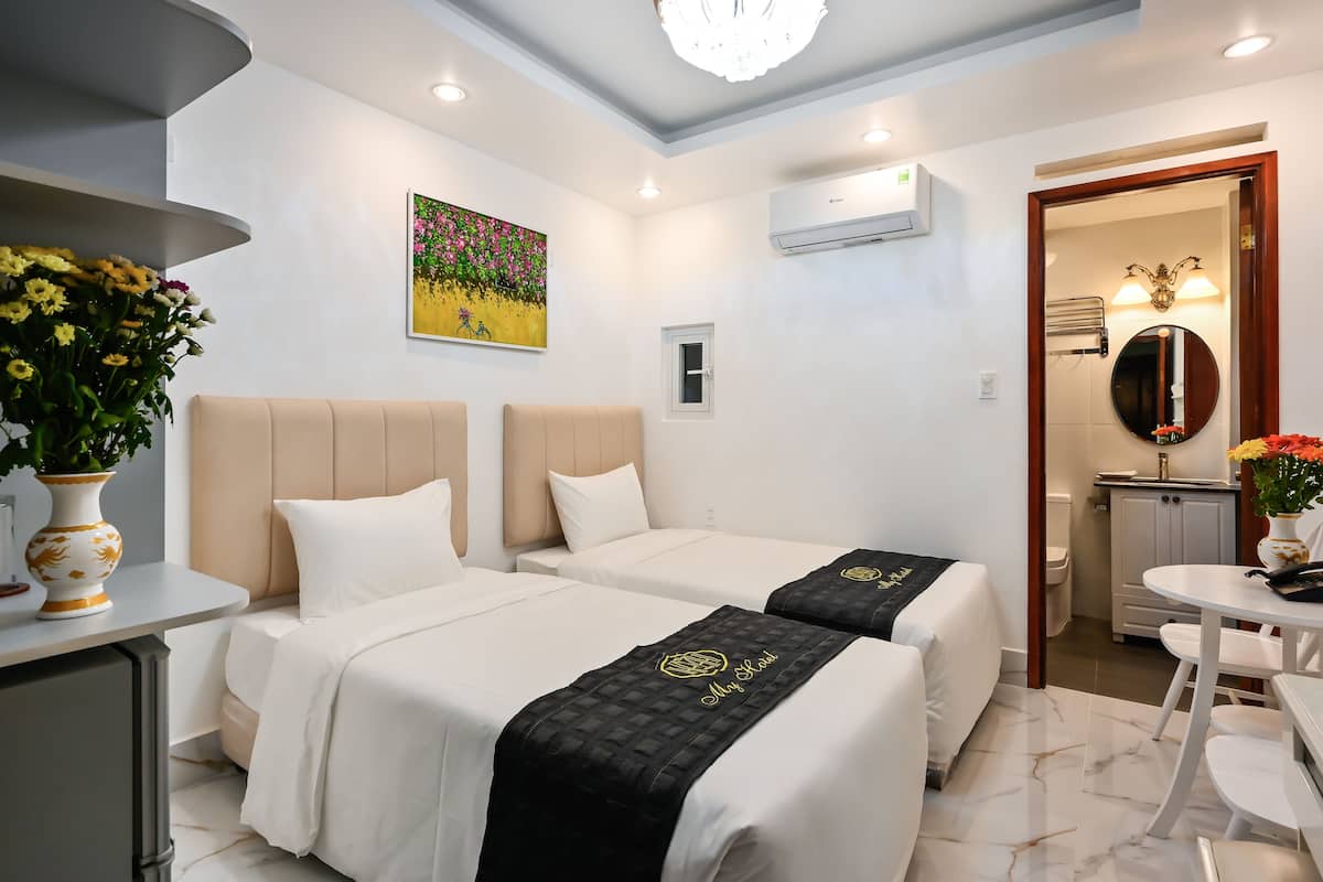 Habitación de hotel con dos camas, un escritorio pequeño, una silla, una mesa de comedor y un baño visible a través de una puerta abierta.