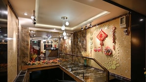 Un vestíbulo de hotel con un mostrador de recepción de mármol, una escalera y una pared decorada con adornos tradicionales chinos.