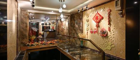 Un vestíbulo de hotel con un mostrador de recepción de mármol, una escalera y una pared decorada con adornos tradicionales chinos.