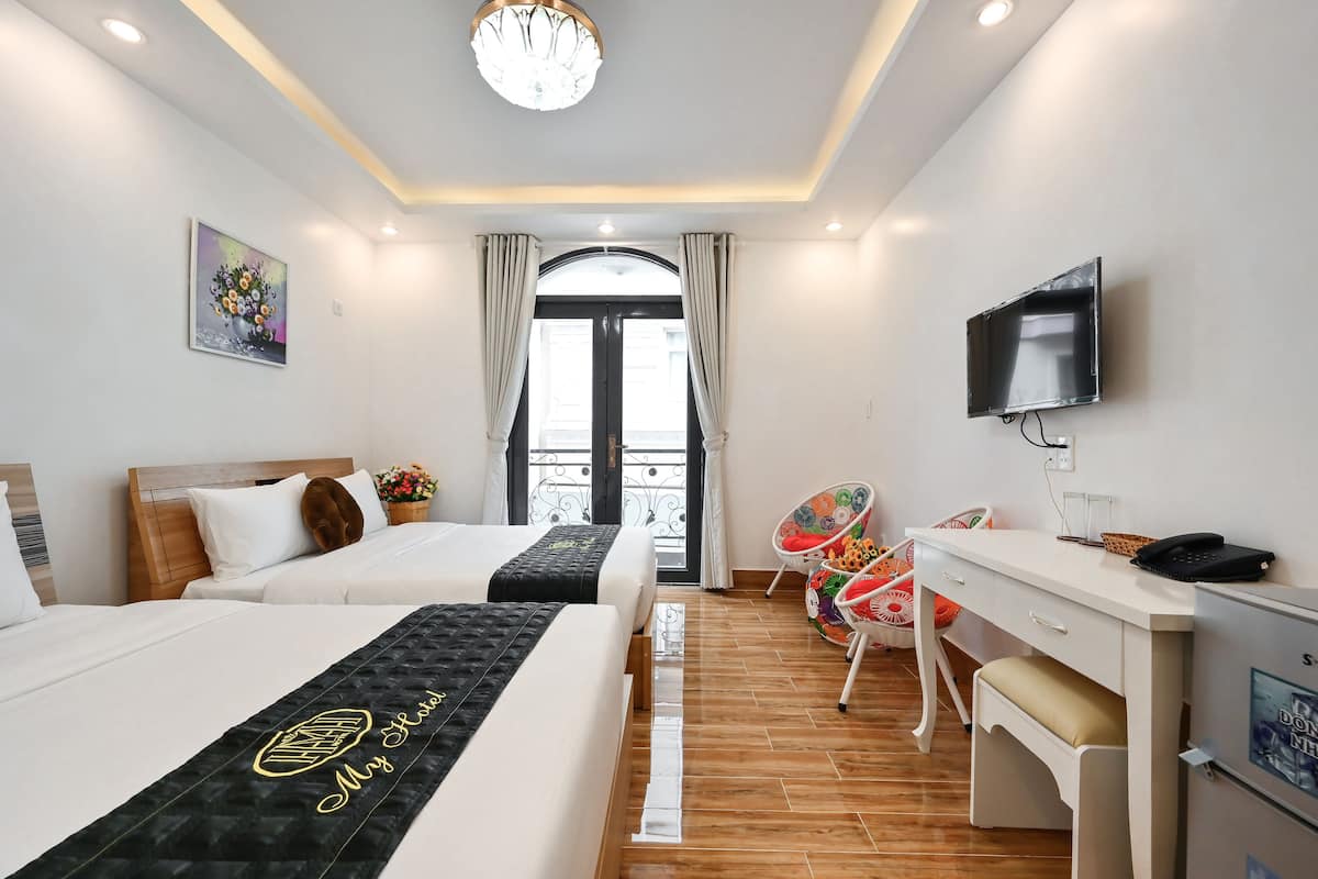 Una habitación de hotel con dos camas, un escritorio, una silla, un televisor y una ventana con cortinas.