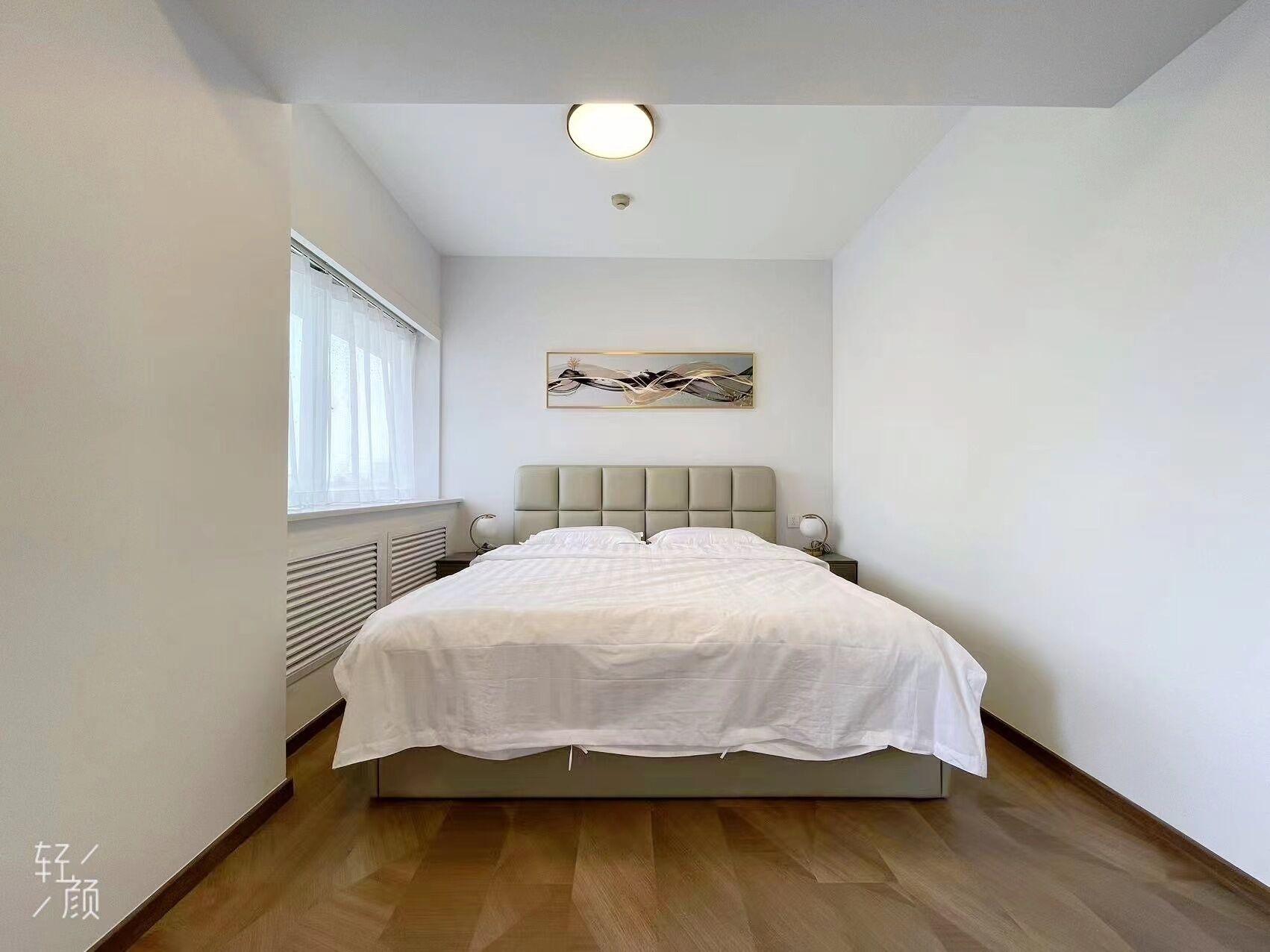 Ein modernes Schlafzimmer mit einem großen Bett, einem Fenster mit durchsichtigen Vorhängen, einem Heizkörper und einer Deckenleuchte.