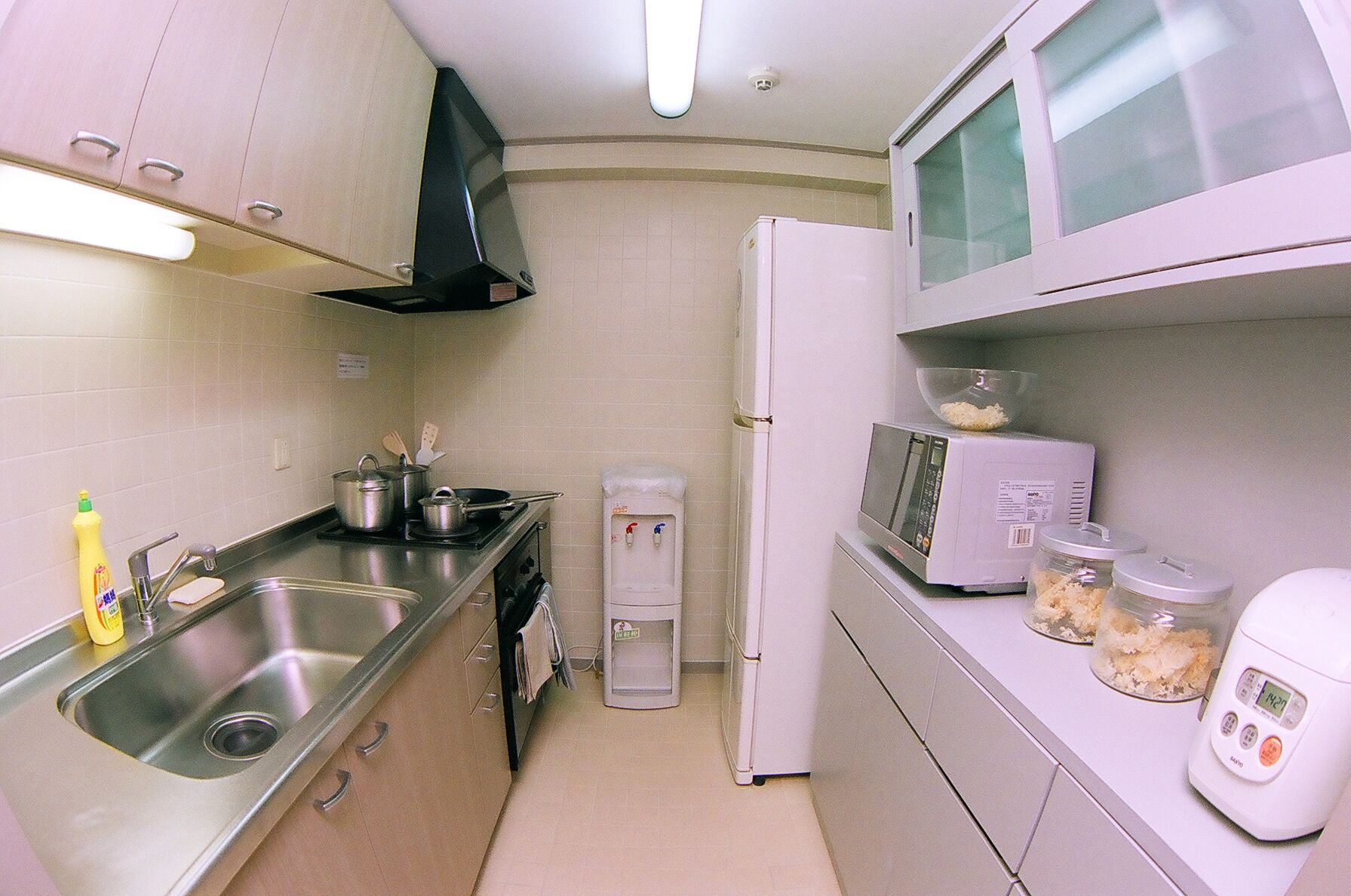 A compact kitchen with stainless steel appliances, a water dispenser, and a microwave.